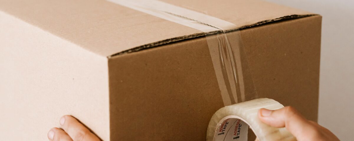 Taxe petits colis : mains scellant un carton d'expédition au ruban adhésif