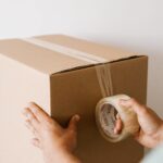 Taxe petits colis : mains scellant un carton d'expédition au ruban adhésif