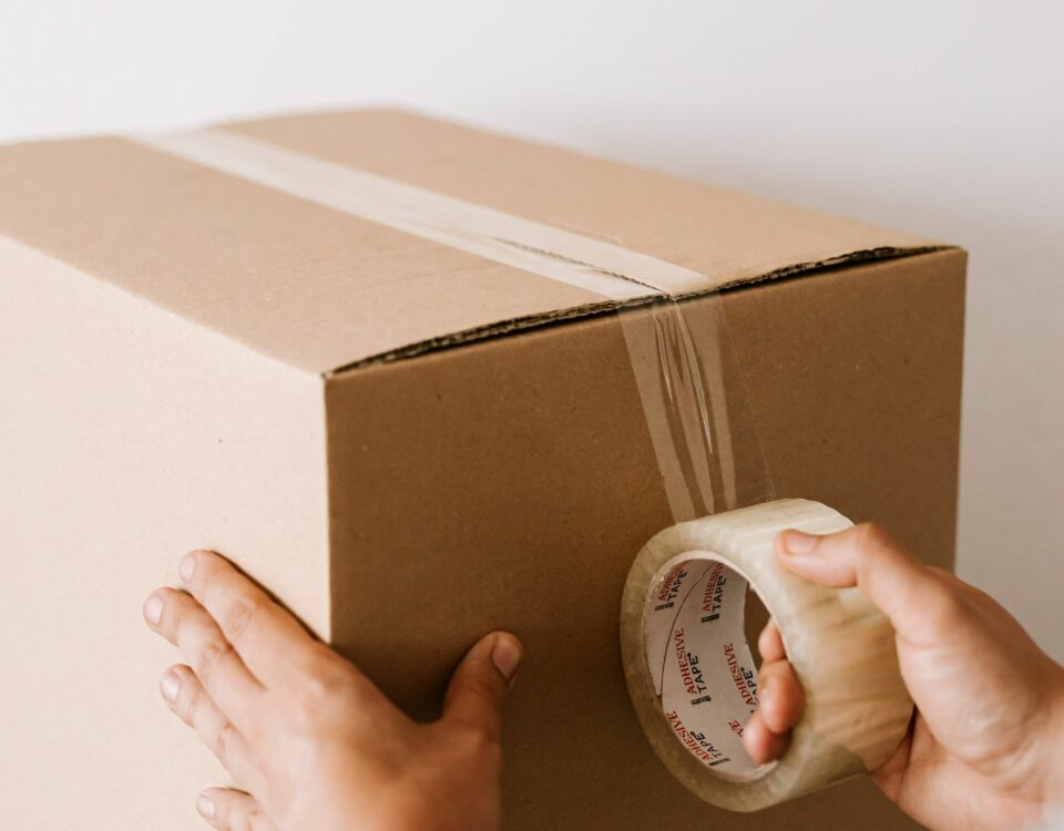 Taxe petits colis : mains scellant un carton d'expédition au ruban adhésif